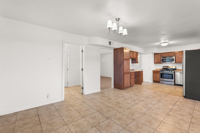 kitchen featuring brown cabinetry, stainless steel appliances, light countertops, a notable chandelier, and light tile patterned flooring