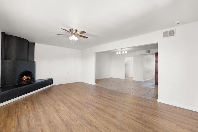 unfurnished living room with light wood-style floors, a large fireplace, visible vents, and ceiling fan with notable chandelier