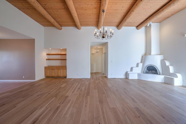 unfurnished living room with a notable chandelier, light wood-style floors, wood ceiling, a large fireplace, and beamed ceiling