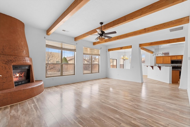 unfurnished living room featuring light wood-type flooring, a large fireplace, visible vents, and ceiling fan with notable chandelier