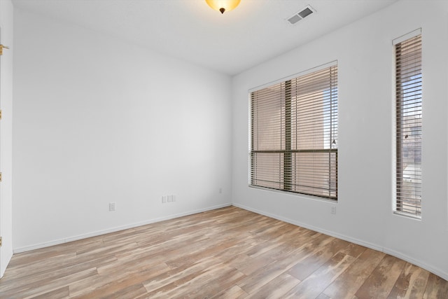 empty room featuring light wood finished floors, visible vents, and baseboards