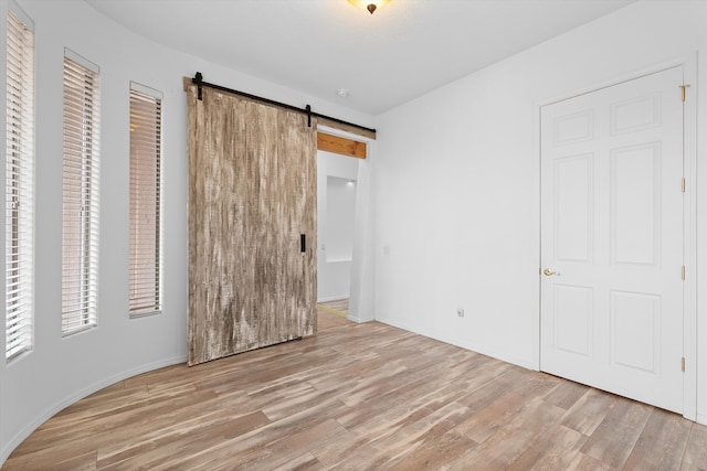 unfurnished bedroom with a barn door and wood finished floors