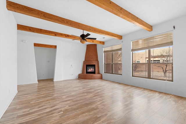 unfurnished living room with a ceiling fan, a fireplace, beamed ceiling, and wood finished floors