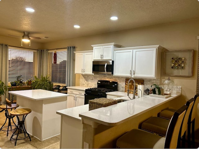 kitchen with tasteful backsplash, white cabinets, stainless steel microwave, a breakfast bar area, and black range with gas stovetop