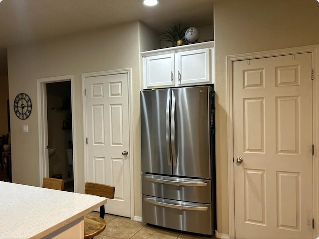 kitchen featuring light countertops, freestanding refrigerator, light tile patterned flooring, and white cabinetry