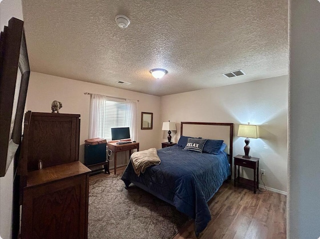 bedroom featuring a textured ceiling, wood finished floors, visible vents, and baseboards