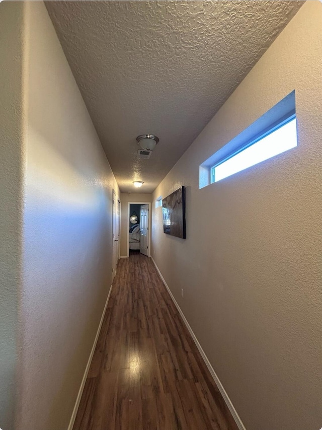 hall with a textured ceiling, wood finished floors, and baseboards