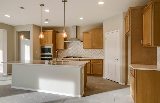 kitchen featuring brown cabinets, visible vents, appliances with stainless steel finishes, a sink, and wall chimney exhaust hood