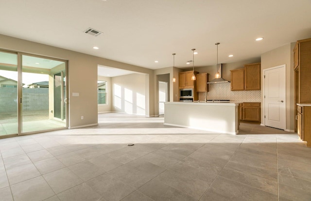 kitchen featuring tasteful backsplash, visible vents, brown cabinetry, wall chimney exhaust hood, and stainless steel microwave