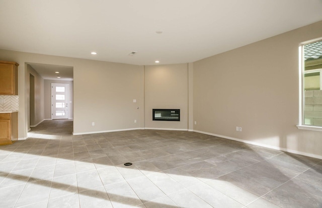 unfurnished living room featuring a glass covered fireplace, light tile patterned flooring, baseboards, and recessed lighting