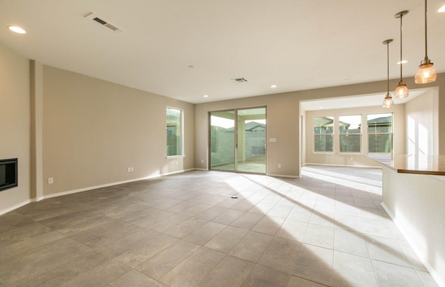 unfurnished living room featuring a glass covered fireplace, visible vents, plenty of natural light, and tile patterned floors