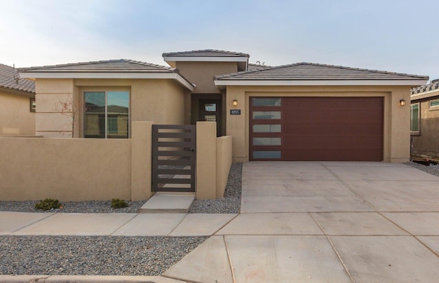 prairie-style house with stucco siding, a gate, fence, a garage, and driveway