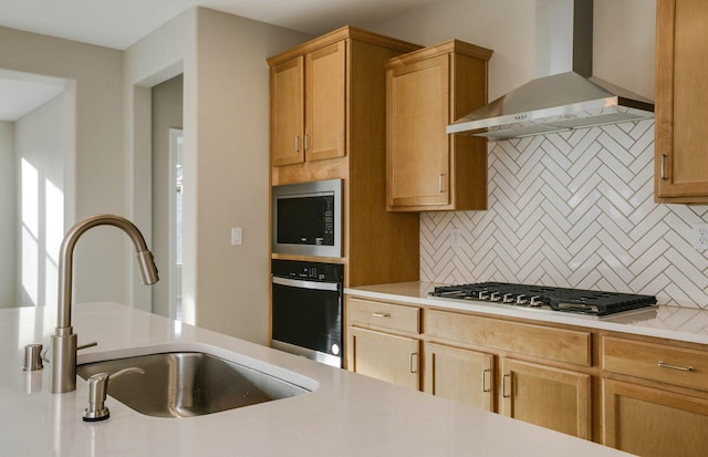 kitchen featuring a sink, light countertops, appliances with stainless steel finishes, decorative backsplash, and wall chimney exhaust hood