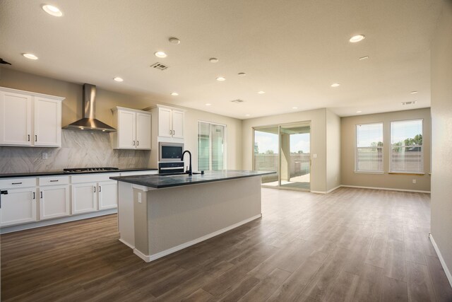 6209 Angelou Ln NW, Albuquerque, NM 87120 - kitchen featuring wall chimney range hood, an island with sink, white cabinets, dark countertops, and recessed lighting