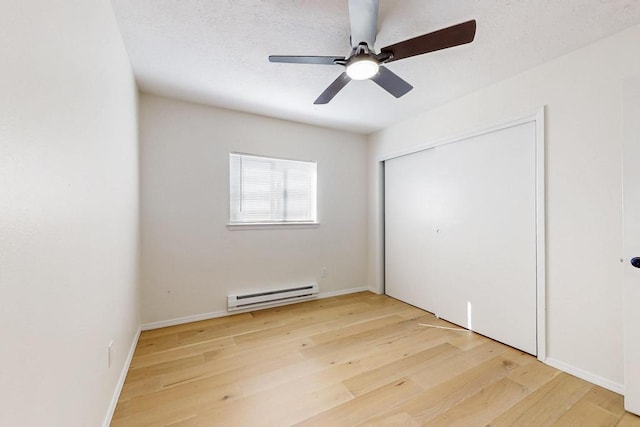 unfurnished bedroom featuring a textured ceiling, light wood-style flooring, a baseboard heating unit, a ceiling fan, and a closet