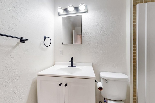 bathroom with toilet, a textured wall, and vanity