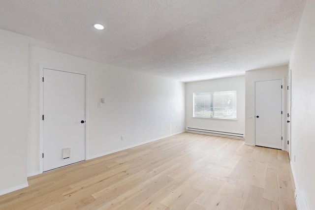 empty room featuring a textured ceiling, a baseboard radiator, baseboards, and light wood-style floors