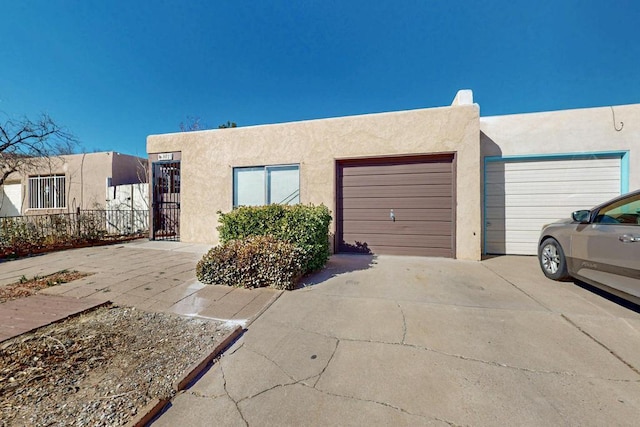 pueblo revival-style home featuring driveway, fence, an attached garage, and stucco siding