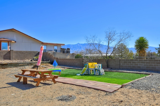 view of yard featuring a mountain view, a playground, and a fenced backyard