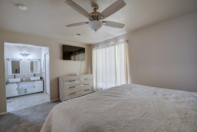 carpeted bedroom with ensuite bath, visible vents, a textured ceiling, and ceiling fan