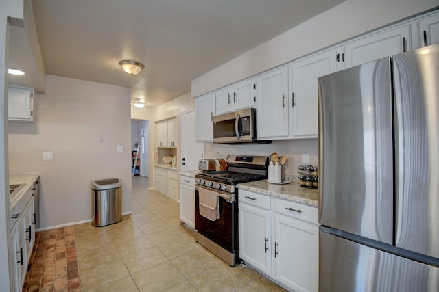 kitchen with light stone counters, appliances with stainless steel finishes, white cabinets, light tile patterned flooring, and baseboards