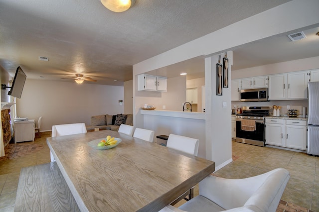 dining area with visible vents, a textured ceiling, baseboards, and a ceiling fan