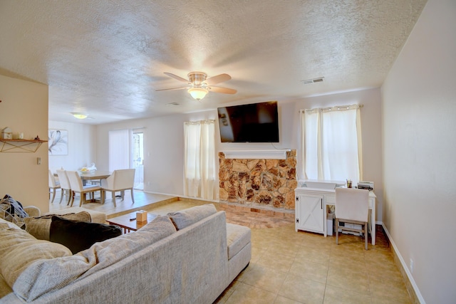 living area featuring visible vents, baseboards, a textured ceiling, and a stone fireplace