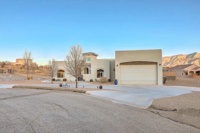 pueblo-style house featuring a tile roof, driveway, an attached garage, and stucco siding