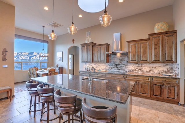 kitchen featuring arched walkways, a sink, visible vents, backsplash, and wall chimney exhaust hood