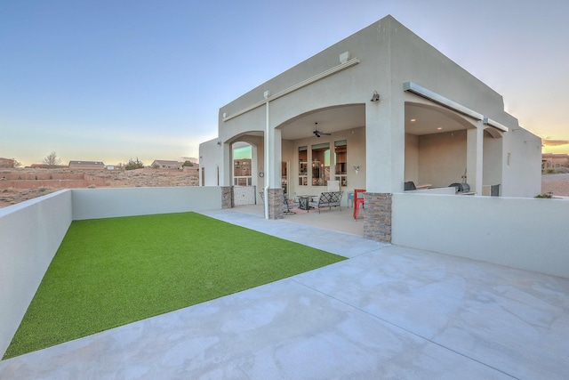 back of house featuring a ceiling fan, a patio, a lawn, and stucco siding