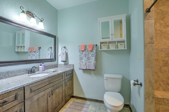 bathroom with baseboards, tiled shower, vanity, and toilet