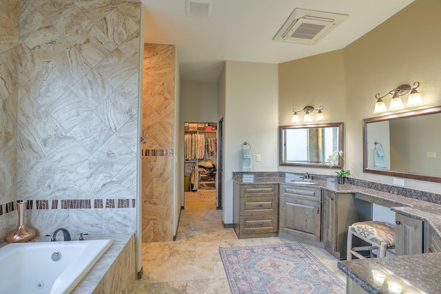 full bathroom featuring a tub with jets, visible vents, a walk in closet, and vanity