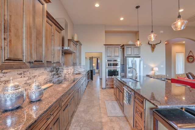 kitchen featuring arched walkways, a sink, appliances with stainless steel finishes, dark stone counters, and tasteful backsplash