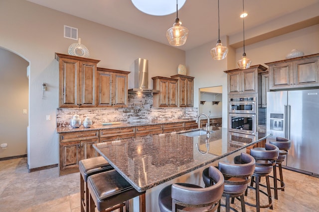 kitchen featuring visible vents, arched walkways, wall chimney exhaust hood, stainless steel appliances, and a sink