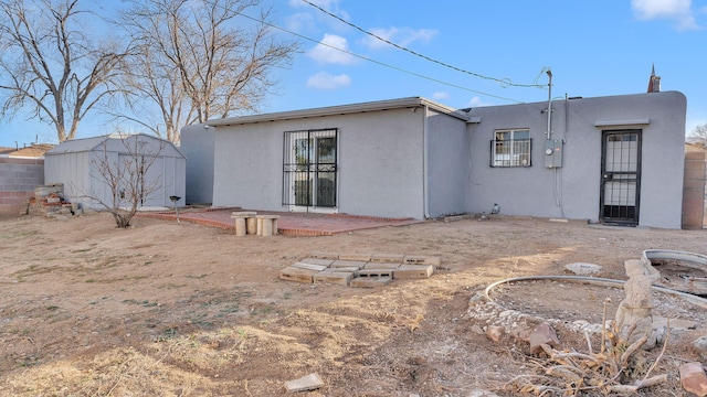 back of property featuring a storage unit, stucco siding, an outbuilding, and fence