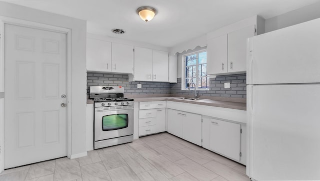 kitchen featuring visible vents, stainless steel gas stove, a sink, freestanding refrigerator, and white cabinets