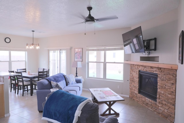 living room with baseboards, light tile patterned floors, ceiling fan with notable chandelier, a fireplace, and a textured ceiling