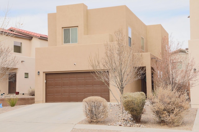 pueblo revival-style home featuring stucco siding, driveway, and an attached garage