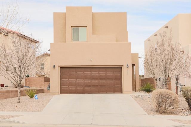 pueblo revival-style home featuring an attached garage, fence, driveway, and stucco siding