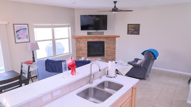 kitchen featuring a ceiling fan, a sink, open floor plan, a fireplace, and light countertops