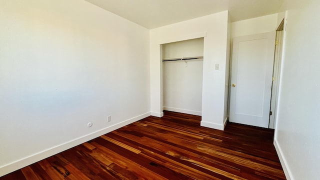 unfurnished bedroom with a closet, dark wood finished floors, and baseboards