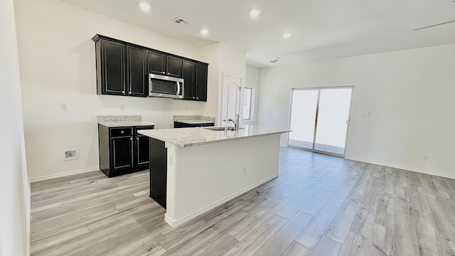 5030 Grace St, Los Lunas, NM 87031 - kitchen with stainless steel microwave, light wood-style flooring, dark cabinets, and recessed lighting