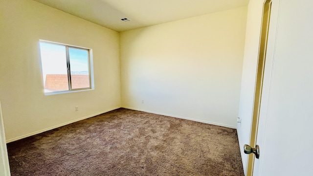 spare room with dark carpet, visible vents, and baseboards