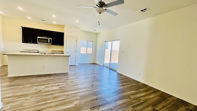 5030 Grace St, Los Lunas, NM 87031 - kitchen with stainless steel microwave, open floor plan, light wood finished floors, dark cabinets, and ceiling fan