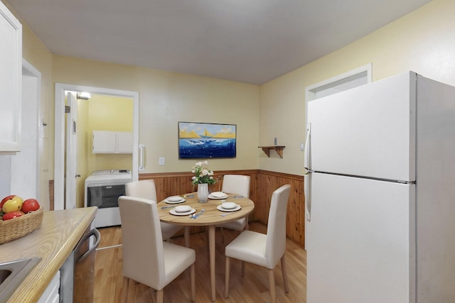 dining area featuring wooden walls, wainscoting, washer / dryer, and light wood-style floors