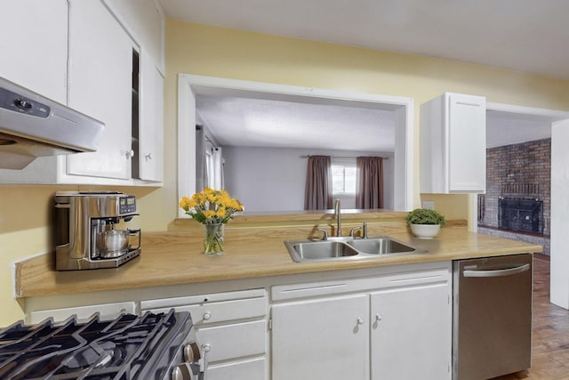 kitchen featuring a fireplace, stainless steel appliances, light countertops, white cabinets, and a sink