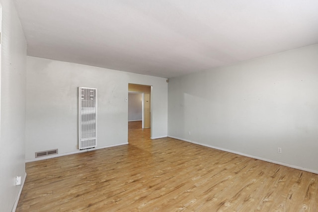 spare room featuring light wood-style flooring, a heating unit, visible vents, and baseboards