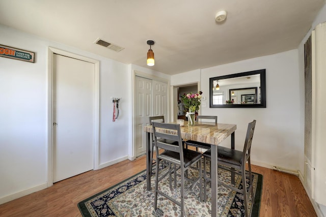 dining space with wood finished floors, visible vents, and baseboards