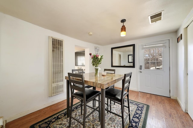 dining area with a heating unit, visible vents, light wood-style flooring, and baseboards