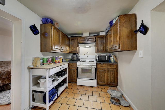 kitchen featuring white range with gas cooktop, baseboards, stainless steel microwave, under cabinet range hood, and light tile patterned flooring